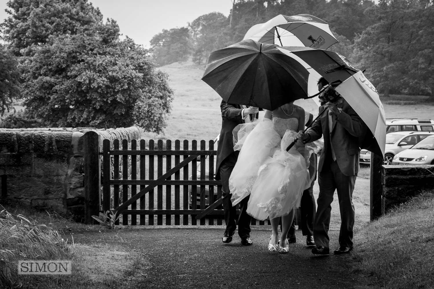 Bride walking int he rain with groomsmen covering her with umbrellas to protect her from the rain